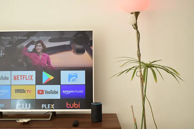 Amazon Alexa lighting a light bulb. Behind a television showing the interface of the Amazon Fire TV

